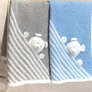 Könnte beinhalten: Zwei gestrickte Babydecken mit weißen Streifen und einem weißen Teddybären, der aus der Ecke jeder Decke schaut. Eine Decke ist grau und die andere ist blau.