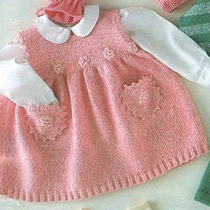 May include: A pink knitted baby dress with a white collar and long sleeves. The dress has a heart-shaped pocket on each side and floral embroidery on the front.