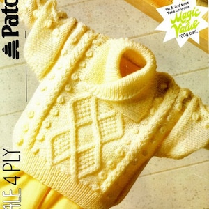 May include: A yellow knitted baby sweater with a diamond pattern and a cable stitch border. The sweater has a mock neck and is made with a 4 ply yarn. The yarn is from Paton's Magic Value line.