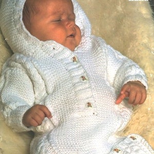 Peut inclure: Combinaison en tricot blanc pour bébé avec une capuche, des boutons et des fleurs brodées. La tenue est conçue pour un bébé de 41 à 51 cm.