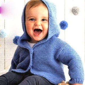 Op de afbeelding: Een baby draagt een blauwe gebreide hoodie met knoopsluiting. De trui is gemaakt van zacht, getextureerd garen.