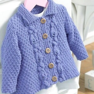 Könnte beinhalten: Hellblau gestrickte Baby-Strickjacke mit Kragen und langen Ärmeln. Die Strickjacke hat Holzknöpfe und ein Zopfmuster auf der Vorderseite. Das Kleidungsstück hängt an einem rosa Kleiderbügel.