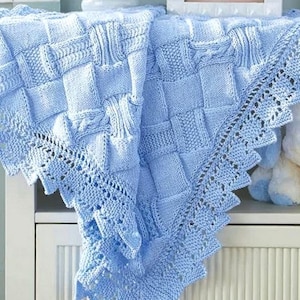 Peut inclure: Une couverture pour bébé en tricot bleu clair avec une bordure en dentelle délicate. La couverture est pliée et exposée sur une étagère blanche.