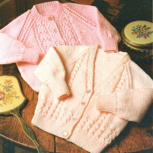 May include: Two knitted cardigans in pink and cream with a cable knit pattern. The cardigans have button closures.