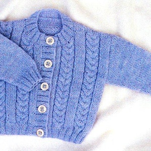 May include: A light blue knitted baby cardigan with a cable knit design. The sweater has long sleeves, a round collar, and five white buttons down the front. The cardigan is made of soft yarn.