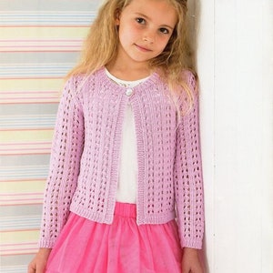 May include: A young girl wearing a light purple knitted cardigan with a white button and a white undershirt. She is also wearing a pink tulle skirt.