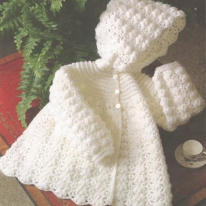 May include: White crocheted baby jacket with a hood and button fastening. The jacket has a scalloped hem and a textured stitch pattern.