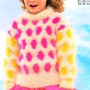 May include: A cream-colored, fuzzy sweater with a high neck, featuring a pattern of large pink and yellow polka dots. The sleeves and lower hem are trimmed with yellow dots. The sweater is paired with a pink skirt.