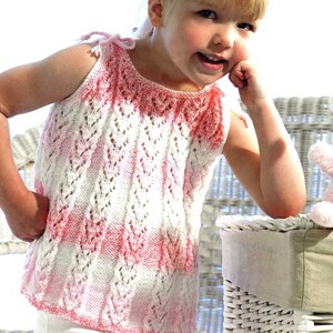 May include: A pink and white knitted sleeveless top with a delicate lace pattern. The top is designed for children ages 18-24 months, with a chest measurement of 18-24 inches.