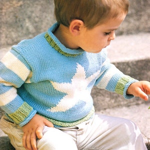 May include: A young child wearing a blue and white striped sweater with a white star on the front. The sweater has green trim around the neck and cuffs.