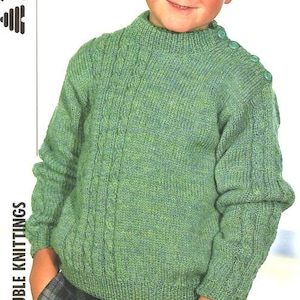 May include: A green knitted jumper with a cable knit pattern and button detailing on the shoulder. The jumper has a high neck and long sleeves.