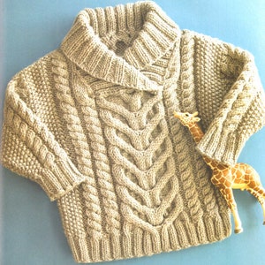 May include: A beige knitted sweater with a cable knit pattern and a wide collar. The sweater is photographed on a light blue background with a toy giraffe.