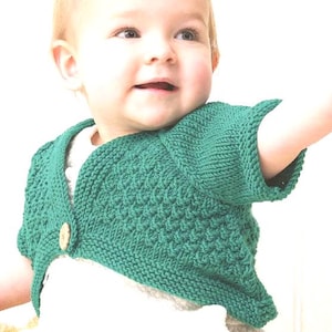 Puede incluir: Un bolero verde tejido para bebé con un patrón texturizado y un cierre de botón de madera único. El suéter de manga corta está diseñado para bebés y niños pequeños. El bolero es de un tono verde vibrante.