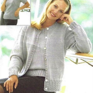 May include: A light gray knitted cardigan with a button closure and a matching knitted top. The cardigan has long sleeves and a ribbed hem and cuffs. The top has short sleeves and a ribbed hem.