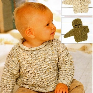 May include: A baby wearing a beige knitted jumper with a textured pattern. The jumper has a round neckline and long sleeves. The baby is sitting on a light brown surface.