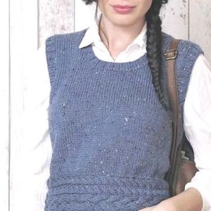 May include: A blue knitted sleeveless vest with a cable knit pattern. The vest is worn over a white shirt and blue jeans.
