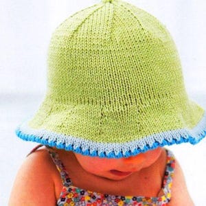 May include: A green knitted sun hat with a blue and white trim. The hat is worn by a child.