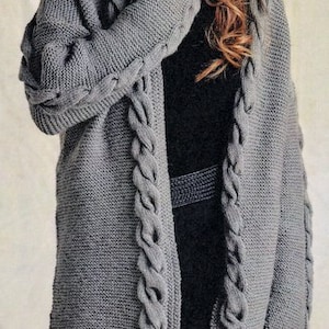 Puede incluir: Un cárdigan de punto gris con un patrón de trenza. El cárdigan tiene un corte largo y holgado y un cuello en V.