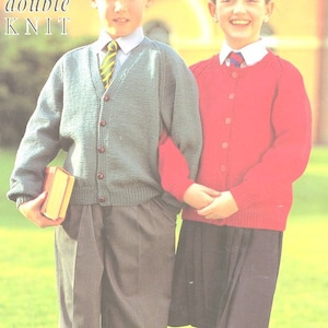 Könnte beinhalten: Zwei Kinder in Schuluniform. Der Junge trägt einen blauen Cardigan mit Knöpfen, eine gelb-grüne gestreifte Krawatte und eine graue Hose. Das Mädchen trägt einen roten Cardigan mit Knöpfen, ein weißes Hemd mit einer schwarzen Krawatte und einen schwarzen Rock. Der Text "double knit" ist im Bild sichtbar.