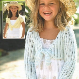 May include: A young girl wearing a light blue crocheted shrug with a white dress underneath. She is wearing a straw hat and has long blonde hair.