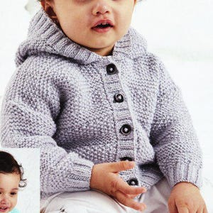 May include: A pale grey, hooded baby cardigan with dark buttons. The knitted sweater has a textured stitch and is buttoned up. The baby is wearing white trousers. The cardigan is a soft, comfortable garment for a baby.