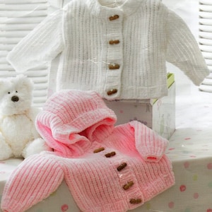Könnte beinhalten: Zwei gestrickte Baby-Cardigans, einer weiß und einer rosa. Der rosa Cardigan hat eine Kapuze und beide Cardigans haben Knöpfe.