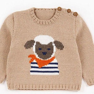 May include: A tan-colored knit sweater featuring a sheep design on the front. The sheep has a white face, brown ears, and is wearing a striped shirt with an orange scarf. The sweater has three wooden buttons on the shoulder.