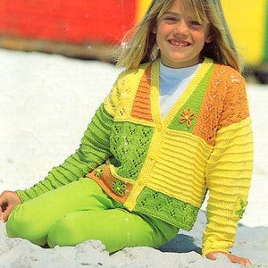 Peut inclure: Une jeune personne portant un cardigan tricoté coloré avec un motif patchwork. Le cardigan a un col en V et est fait de différentes nuances de jaune, de vert et d'orange. Le cardigan présente un motif floral sur le devant.