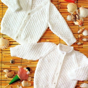 May include: Two white knitted baby cardigans with button closures. The cardigan on top has a V-neck and the cardigan on the bottom has a round neck.