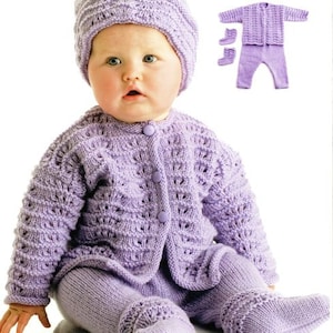 May include: A baby wearing a lavender knitted outfit, including a hat, cardigan, pants, and booties. The outfit is made with a delicate stitch pattern.