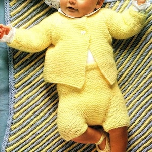 Puede incluir: Un conjunto de bebé de punto amarillo con un cárdigan y pantalones cortos. El conjunto está colocado sobre una manta rayada azul y amarilla.