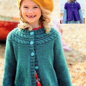 Op de afbeelding: Een tealblauwe gebreide cardigan met een kabelbreipatroon en turquoise knopen. De cardigan wordt gedragen over een rode bloemenjurk en een gele baret.