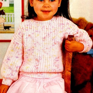 Puede incluir: Un suéter de punto rosa y blanco con cuello redondo. El suéter tiene un patrón moteado con hilo rosa, blanco y amarillo.