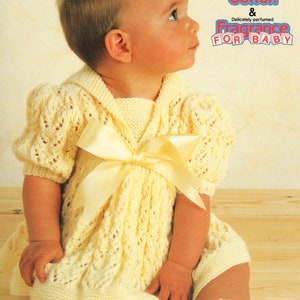 Puede incluir: Una niña pequeña con un vestido blanco de punto con un lazo amarillo. El vestido tiene un delicado patrón de encaje. El texto "Cotton & Delicately perfumed Fragrance For Baby" está en la esquina superior derecha de la imagen.