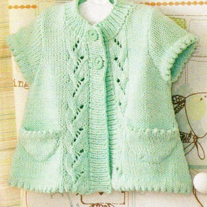 May include: A light green, knitted cardigan with short sleeves and two front pockets. The cardigan features a round collar and is fastened with two buttons. The knit design includes decorative openwork patterns.
