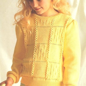 May include: A yellow knitted sweater with a textured, geometric design. The sweater has long sleeves and a ribbed hem and cuffs. The sweater is worn by a person with blonde hair and is paired with floral patterned pants.