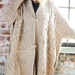 May include: A beige knitted cardigan with a cable knit pattern and floral embellishments. The cardigan has a shawl collar and a button closure.