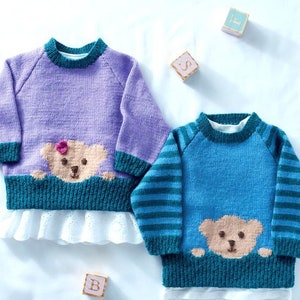 Op de afbeelding: Twee gebreide babytruien met teddybeer-applicaties. De ene trui is paars met een teal beer en de andere is blauw met een teal beer.