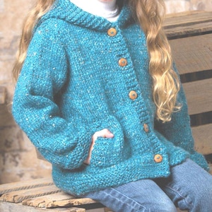 May include: Teal hooded cardigan with wooden buttons and pockets. The chunky knit sweater has a textured appearance and is worn with blue jeans. The cardigan is a cozy, handmade garment.