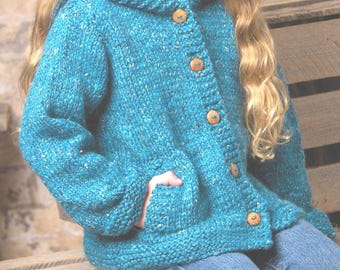 Op de afbeelding: Turquoise vest met capuchon, houten knopen en zakken. De dikke gebreide trui heeft een textuur en wordt gedragen met een blauwe spijkerbroek. Het vest is een comfortabel, handgemaakt kledingstuk.