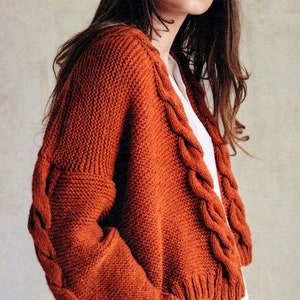 Könnte beinhalten: Ein rostiger Strickpullover mit Zopfmuster. Der Pullover hat einen V-Ausschnitt und lange Ärmel.