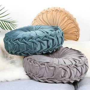 May include: Three round floor cushions in different colors. The cushions are made of a soft, plush fabric with a quilted design. The cushions are beige, teal, and gray.