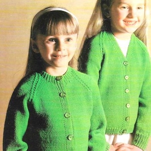 May include: Two girls wearing green knitted cardigans with button closures. The cardigan on the left has a round neckline, while the cardigan on the right has a V-neckline.