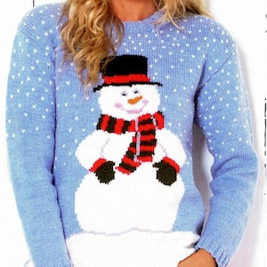 Op de afbeelding: Een lichtblauwe gebreide trui met een wit sneeuwpopontwerp. De sneeuwpop draagt ​​een zwarte hoge hoed, een rood-zwarte gestreepte sjaal en zwarte wanten. De trui heeft een wit sneeuwvlokkenpatroon.