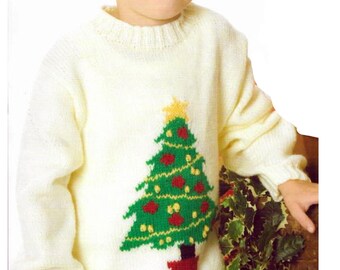 May include: A cream-colored knitted sweater featuring a green Christmas tree design with red ornaments and a yellow star. The sweater has a ribbed hem and cuffs, perfect for the holiday season. The child is wearing the sweater.