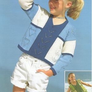 May include: A young girl wearing a blue, white, and cream knitted sweater with a geometric pattern. She is wearing white denim shorts and has her hair pulled back in a ponytail.