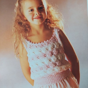 May include: A young girl wearing a pink and white crocheted sleeveless top with a white flower in her hair.