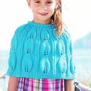 May include: A turquoise blue knitted cape with a leaf pattern. The cape features a round neckline and a series of oval-shaped designs with small openings. The cape is worn over a pink and white plaid dress.