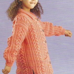 May include: A coral cable-knit cardigan with a collared neckline and button closure. The sweater has a pocket on the front and is worn by a child. The sleeves are long and the hat is blue.