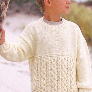May include: A white knitted sweater with a cable knit pattern on the bottom half. The sweater has a crew neck and long sleeves.